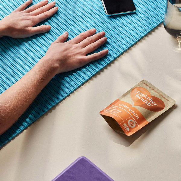 Zwei Hände auf einer Sportmatte, daneben liegt eine Tüte Together Health Curcumin