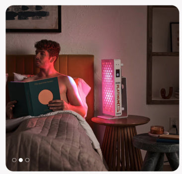 Ein Mann sitzt im Bett und lässt sich von einer Rotlichtlampe bestrahlen